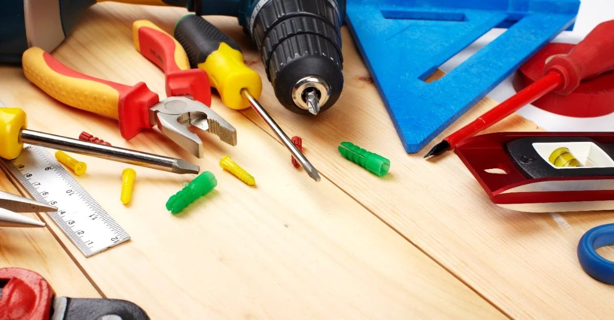 A collection of tools that could be used by a handyman in Crowley, TX, including a power drill, carpenter’s square, several screwdrivers, a level and a pair of pliers.