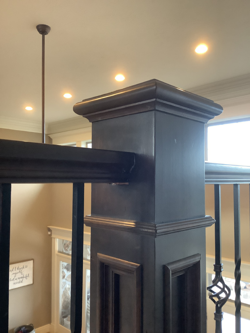 A section of stair railing with a column that has elaborate trim and finish carpentry added on the top and sides.