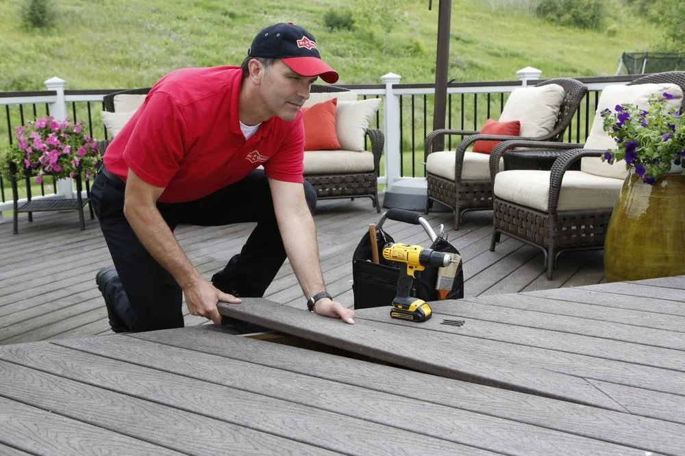 A handyman from Mr. Handyman installing a replacement deck board while providing services for deck maintenance.