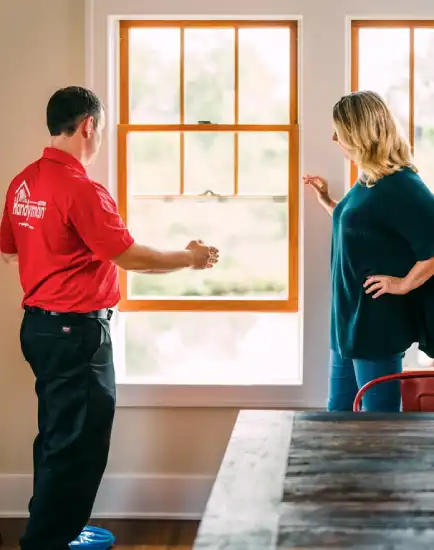 Mr. Handyman technician standing in front of window with homeowner and using hands to show the width of the window.