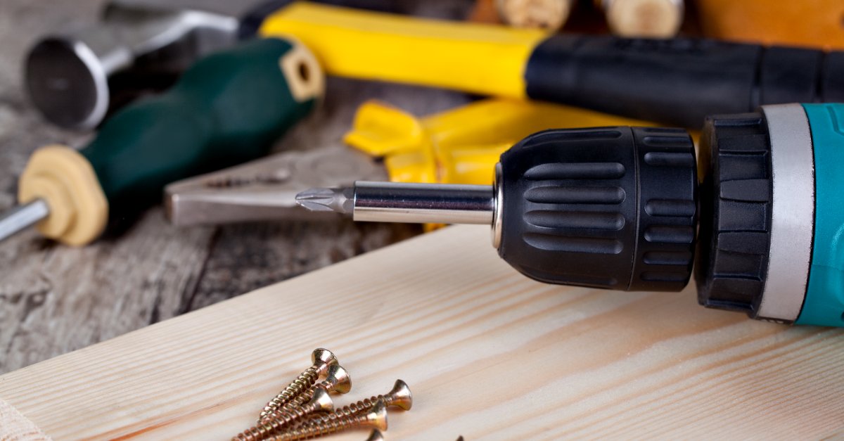 A drill and screws lying on a wood board with a set of tools in the background ready to be used by a handyman in Shiloh, IL.