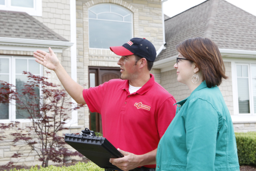 A handyman dressed in the Mr. Handyman uniform speaking with a homeowner about the exterior of their home.