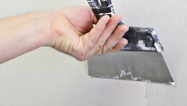 A handyman using a wide putty knife to spread joint compound over a hole in a wall during drywall repairs.