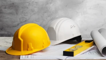 Two hardhats, a level, and several diagrams for renovation plans laid out on a table for use by a general contractor in Dallas, TX.