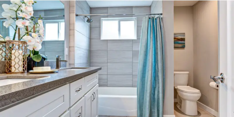 A completed bathroom remodel with large shower tiles, a wide mirror, and white cabinets.