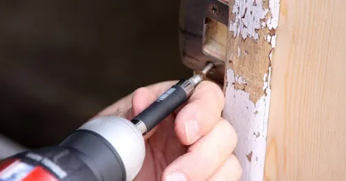 A handyman using a power drill to replace the strike plate on the frame of an interior doorway.
