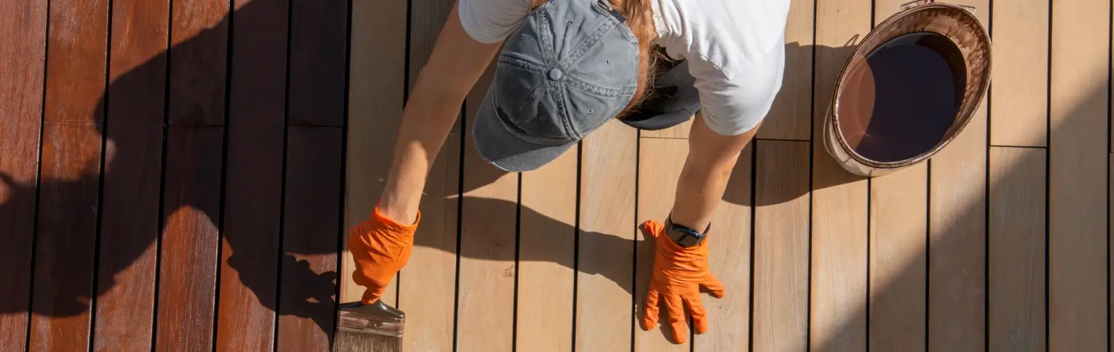 A person wearing orange gloves applies stain to deck boards.