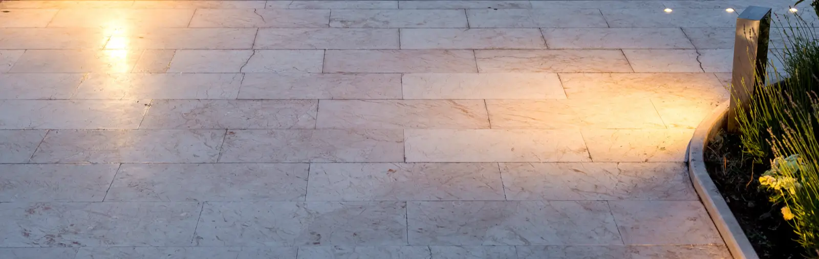 Outdoor area featuring a neatly arranged, elegant rectangular natural stone flooring illuminated softly with warm exterior lights and bordered by decorative greenery, showcasing an aesthetically pleasing stone paving option.