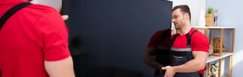 Two handymen lifting and positioning a large flat-screen TV onto a wall mount