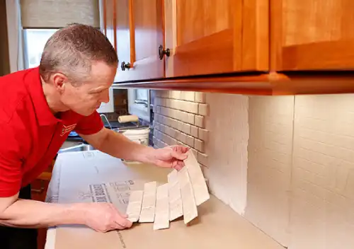 Mr. Handyman technician installing a tiled backsplash in a kitchen.