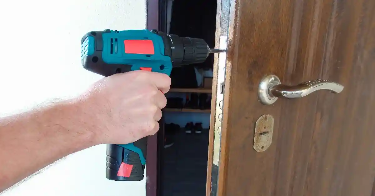 A handyman using a power drill to fix the strike plate of a door’s lock during an appointment for door repairs in Vancouver, WA.