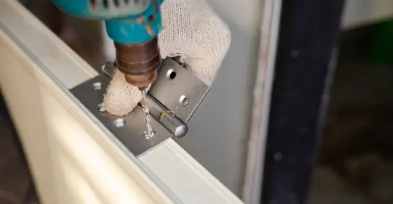 A handyman using a drill to create holes for door hinges on the side of a door slab during an appointment for door installation services.