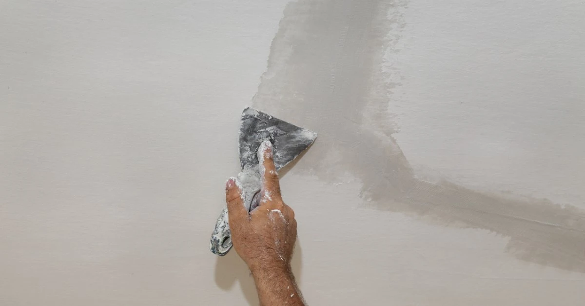 Mr. Handyman service professional using a putty knife to spread drywall compound on a ceiling.
