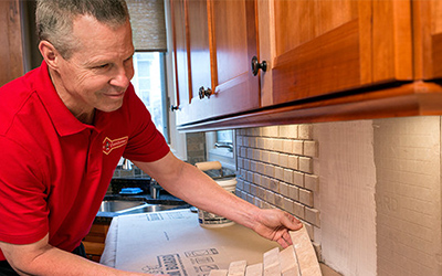 A courteous Mr. Handyman tech installing new kitchen backsplash