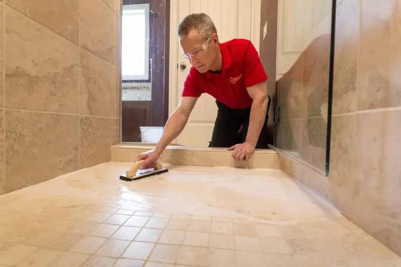 A handyman from Mr. Handyman using a trowel to spread tile cleaner across the surface of a tiled shower floor.