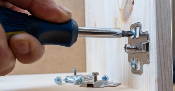 A handyman using a screwdriver to install new cabinet door hinges during an appointment for cabinet repair in Frisco, TX.