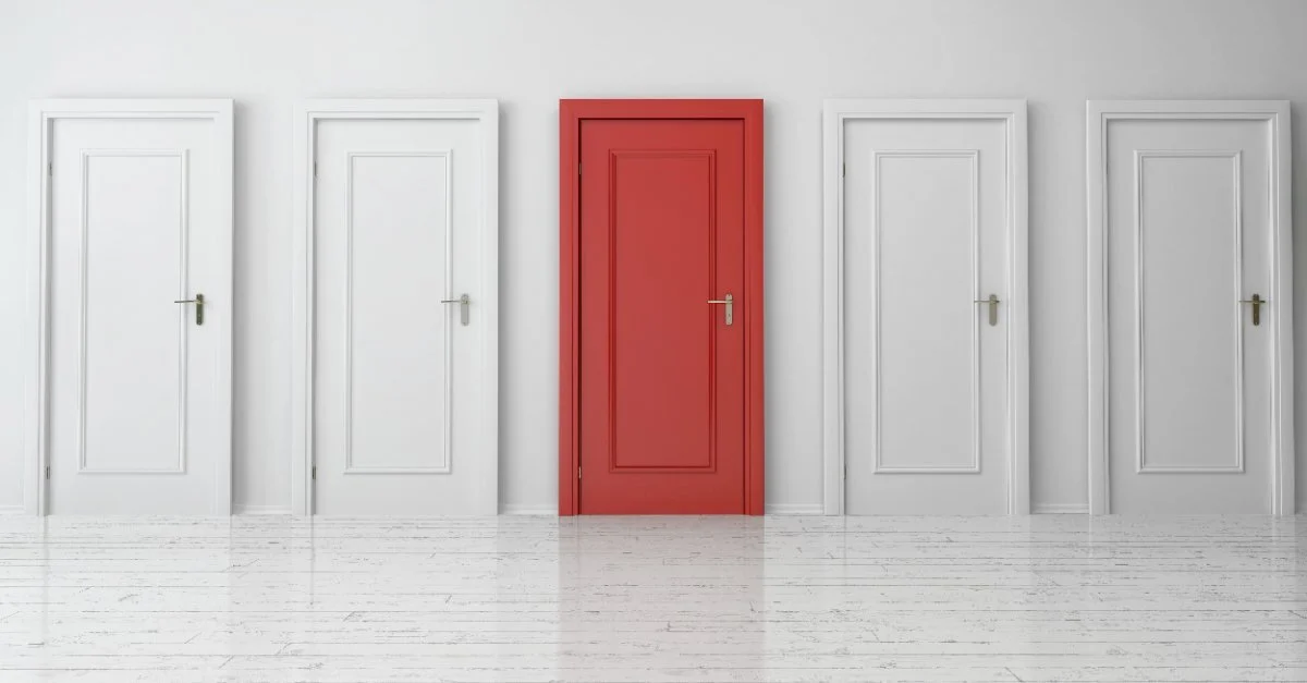 A row of white doors on a white wall with one red door in the middle of the row, all of which could be installed with services for door installation in Naples, FL. 