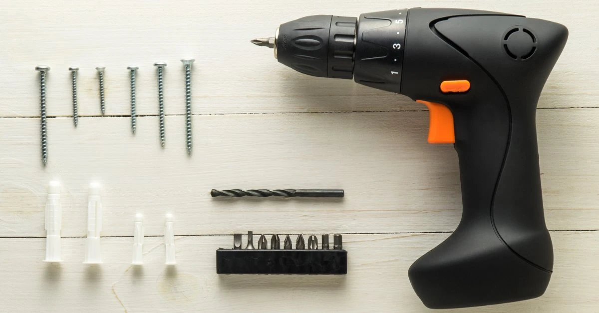 A collection of tools and parts commonly used for picture hanging in Wichita, KS, including a power drill, screws of several sizes, a drill bit and drywall anchors.