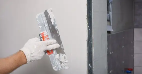 A handyman using a flat putty knife to spread joint compound over a wall with recently completed drywall repairs in Colorado Springs.
