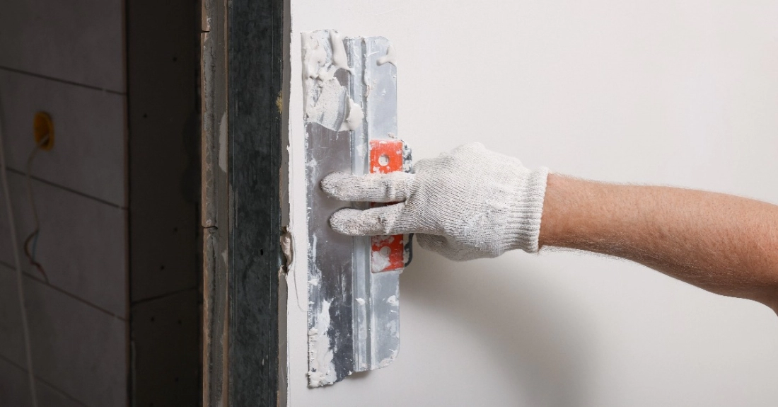 A handyman using a putty scraper to spread fresh compound over a wall after completing drywall repairs in Knoxville, TN.