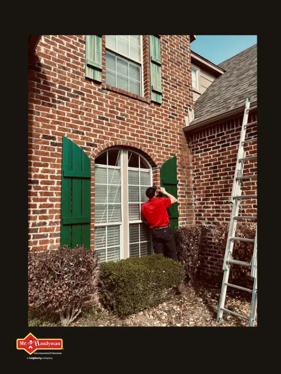 A handyman examining a tall window’s shutters during an appointment for window repair in Tulsa, Oklahoma