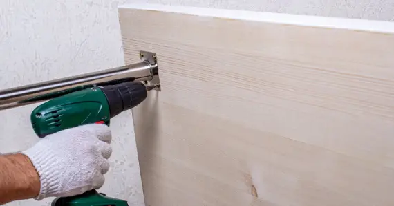 A handyman using a power drill to attach a metal table leg to the bottom side of a table while completing a furniture assembly project as a commercial handyman in Fairfield, CT.