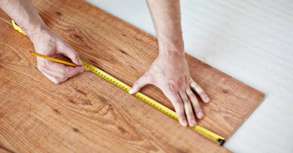A handyman using a tape measure to measure out material for flooring installation in Wichita, KS.