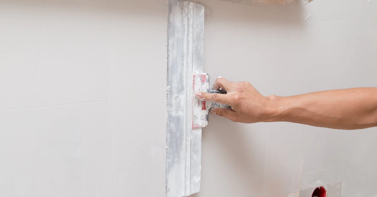 A handyman smoothing out drywall repair compound along a wall during an appointment for drywall repair in Frisco, TX