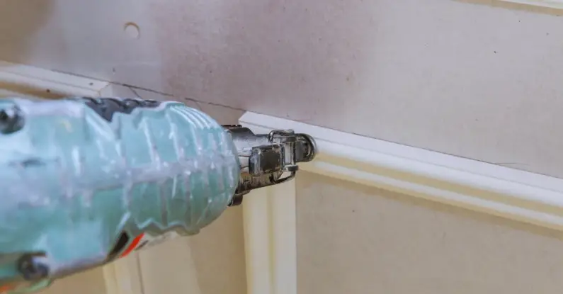 A handyman using a nail gun to attach thin sections of trim to a wall during an appointment for trim installation in Frisco, TX.