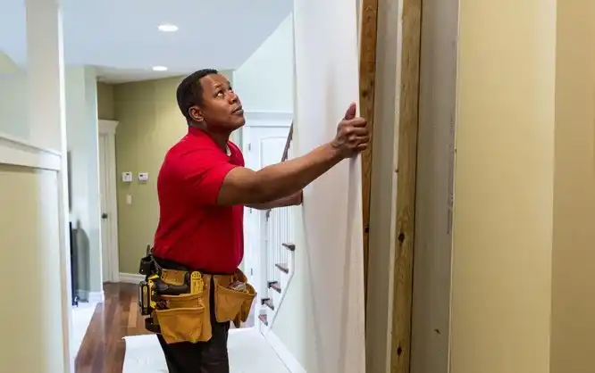 A handyman from Mr. Handyman lifting a new drywall sheet into place inside of a home during an appointment for drywall installation service.