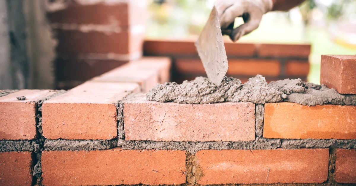 A handyman using a trowel to lay and spread mortar across a short brick wall during while providing services for masonry in Wichita, KS.