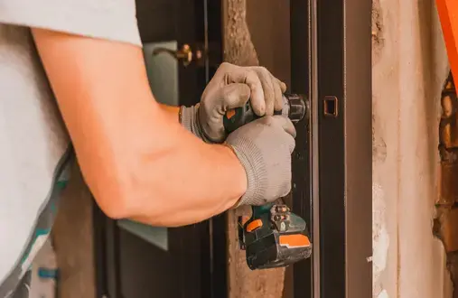A handyman using a drill to install a metal door frame while completing door installation for the front door of a home.