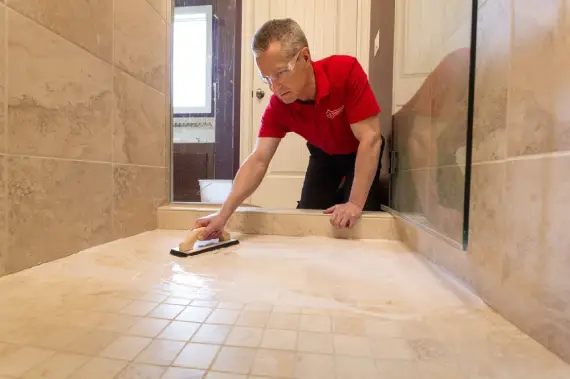 A handyman in the process of sealing a shower floor after completing tile installation in Lehi, UT.