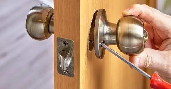 A handyman using a screwdriver to install a new doorknob while providing services for door repairs in Walpole, MA. 
