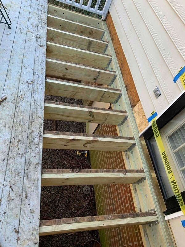 An old deck with several boards removed near the wall of the home its attached to during an appointment for repairs.