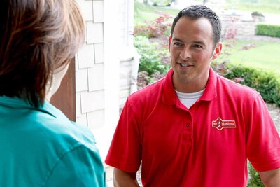 A uniformed Mr. Handyman tech greeting a customer at her front door