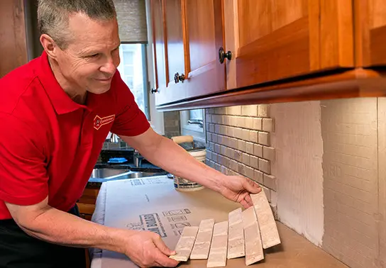 A handyman from Mr. Handyman installing tile sheets on a kitchen wall during an appointment for kitchen backsplash installation.