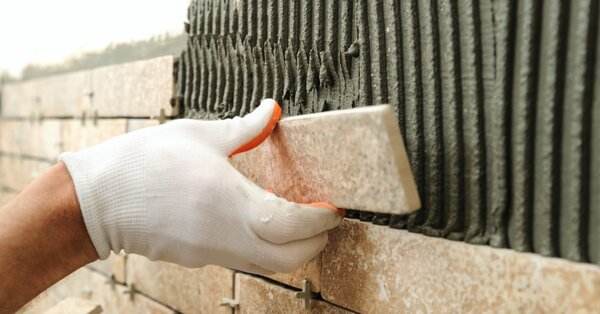 A handyman installing new tile on the side of a wall where mortar has already been applied prior to tile installation.