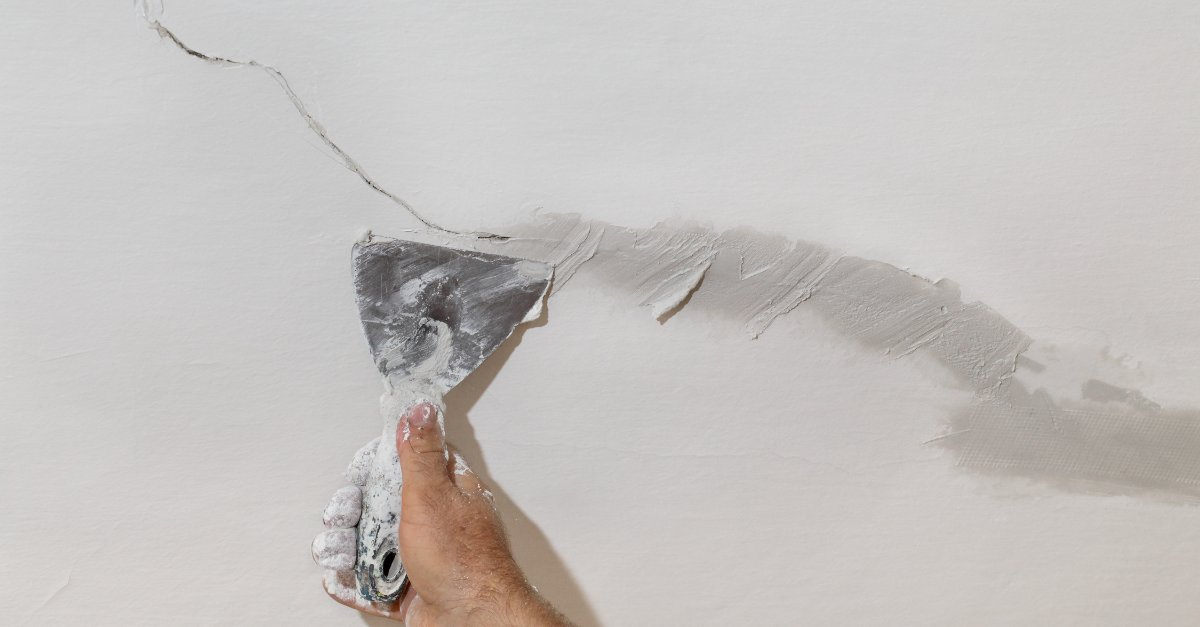 A handyman using a putty knife to apply joint compound along a crack in a wall during an appointment for drywall repair in Boulder, CO.
