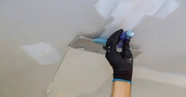 A handyman using a trowel to spread Spackle on a ceiling for ceiling repairs in Flower Mound, TX.
