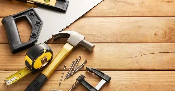 A group of tools commonly used for Dallas carpentry service lying on wooden boards, including a level, hand saw, hammer, tape measure, clamp and nails.