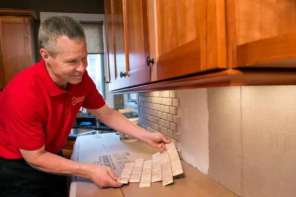 A handyman from Mr. Handyman installing tile sheets on a backsplash during a kitchen remodel in Frisco, TX.