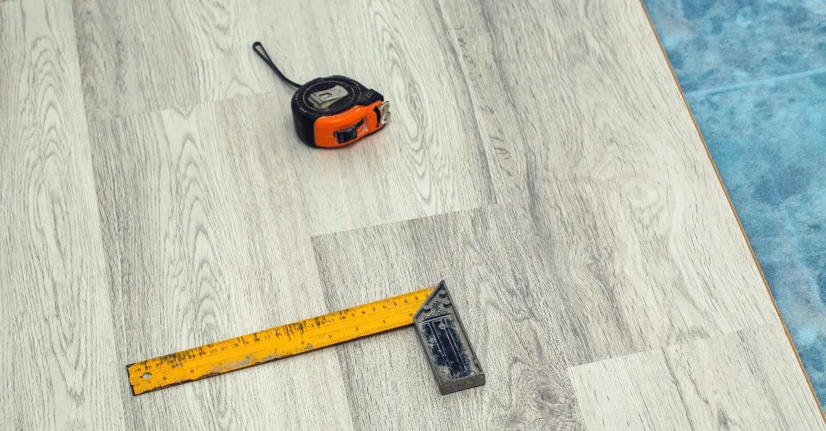 A ruler and a tape measure lying on a section of laminate flooring that has just been refinished with floor repairs.