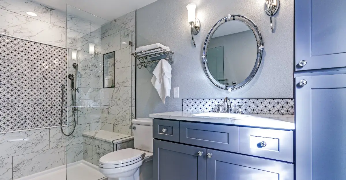  A newly remodeled bathroom with light-blue cabinets, white marble shower tiles and a glass shower enclosure.