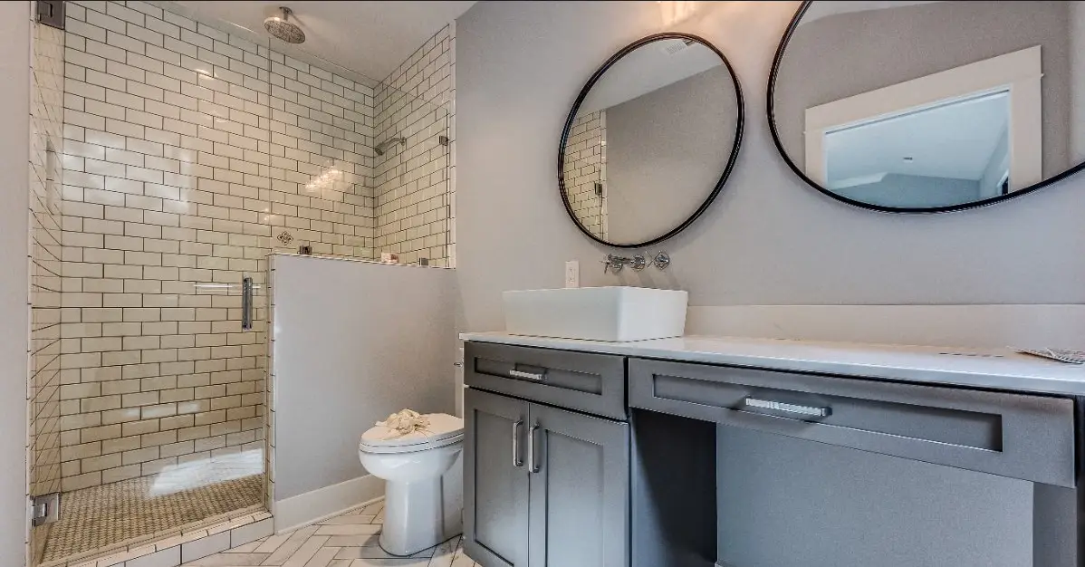 A modern bathroom with subway tile, circular mirrors, a low clearance cabinet, and other features that are popular in Cincinnati bathroom remodel projects.