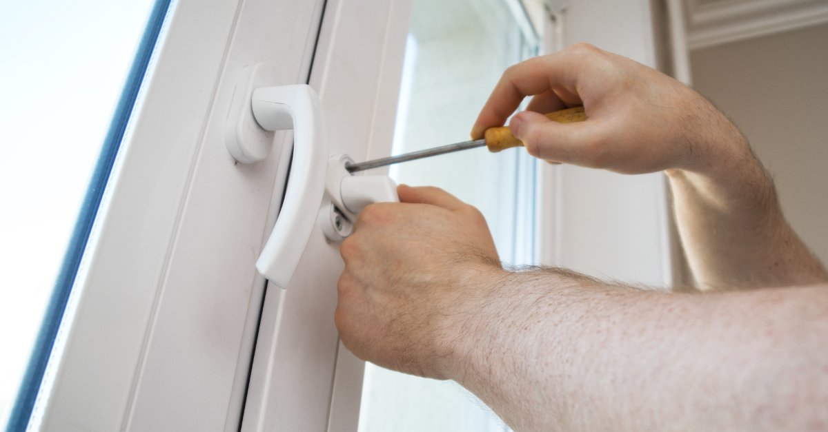 A handyman using a screwdriver to fix the latching mechanism on a casement window.