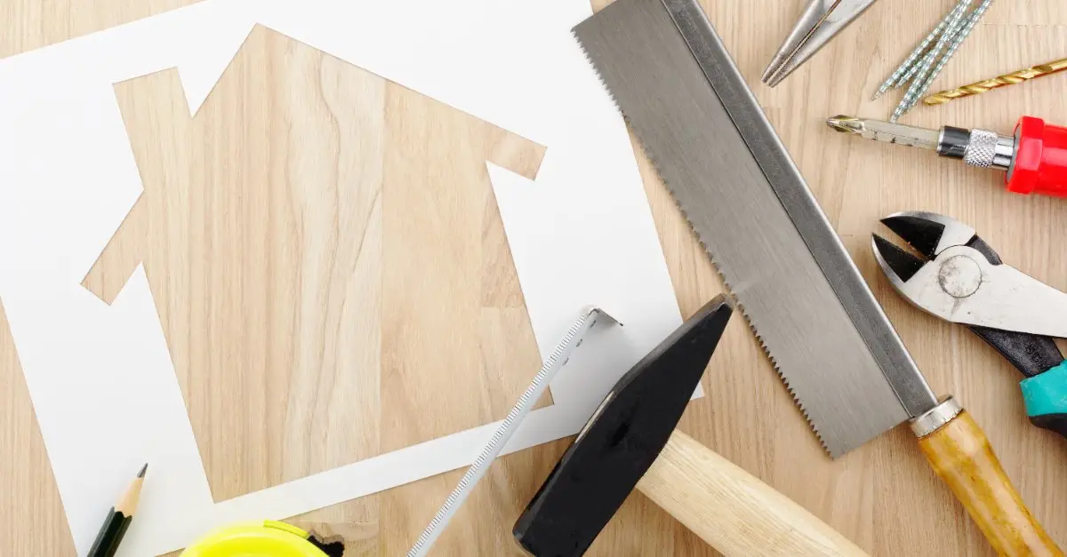 A variety of tools used for home improvement in McKinney arranged on a wood surface next to a piece of paper with the shape of a house cut out of it.