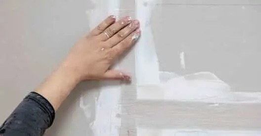A hand smoothing out joint tape being used for McKinney drywall repair services.