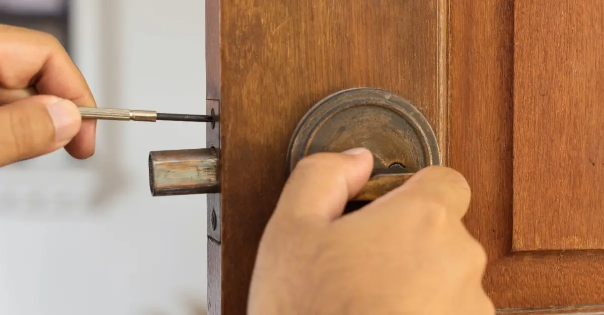 A close-up of a handyman screwing in a new strike plate on a wooden door during an appointment for interior door repair in Naples, FL.