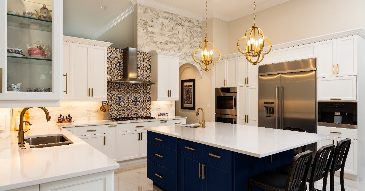 A newly remodeled kitchen with white cabinets, an island, hanging lights, and a mosaic tile backsplash.